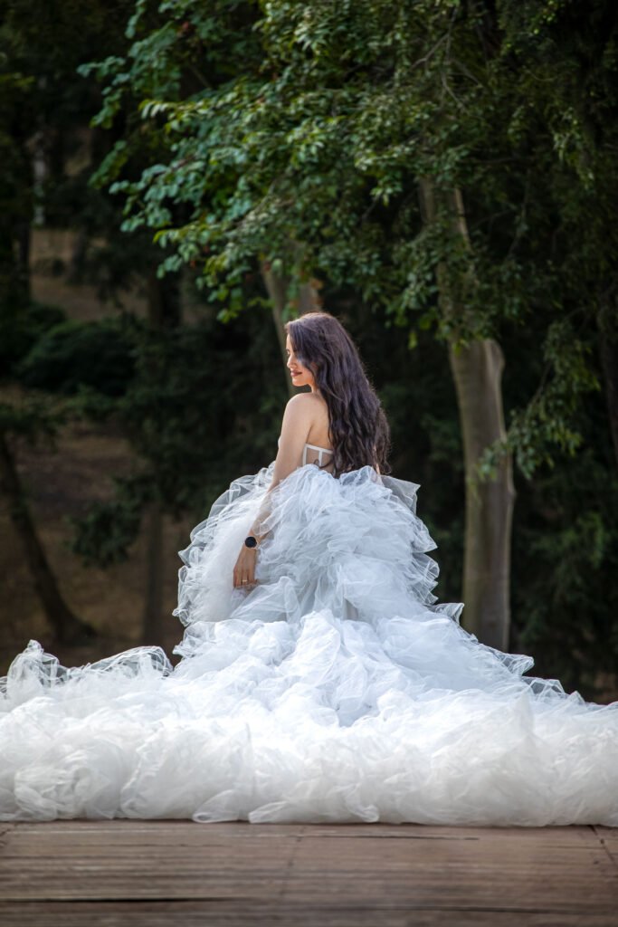 Elegant bride in a voluminous white tulle gown looking over her shoulder in a lush green forest setting in Istanbul