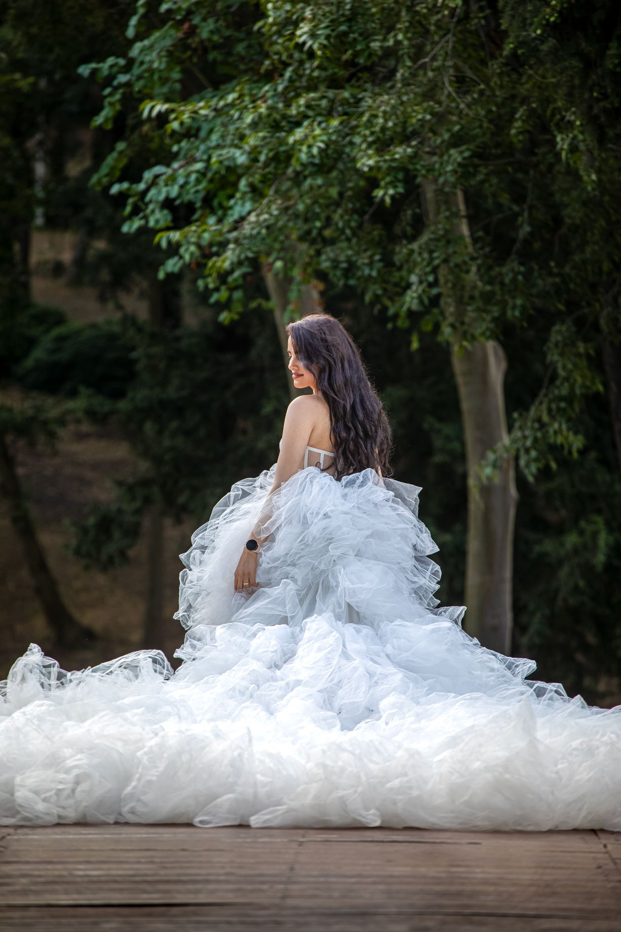 Elegant bride in a voluminous white tulle gown looking over her shoulder in a lush green forest setting in Istanbul
