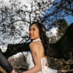 Smiling Asian bride in a lace wedding dress holding hands with groom during outdoor wedding photoshoot